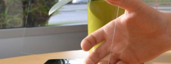 Image of a hand holding a small sample of Ubiquitous Energy's transparent, solar-generating glass (EPIC Agreement EPC-18-004)